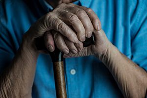 dim lighting close up of elderly hands resting on walking cane